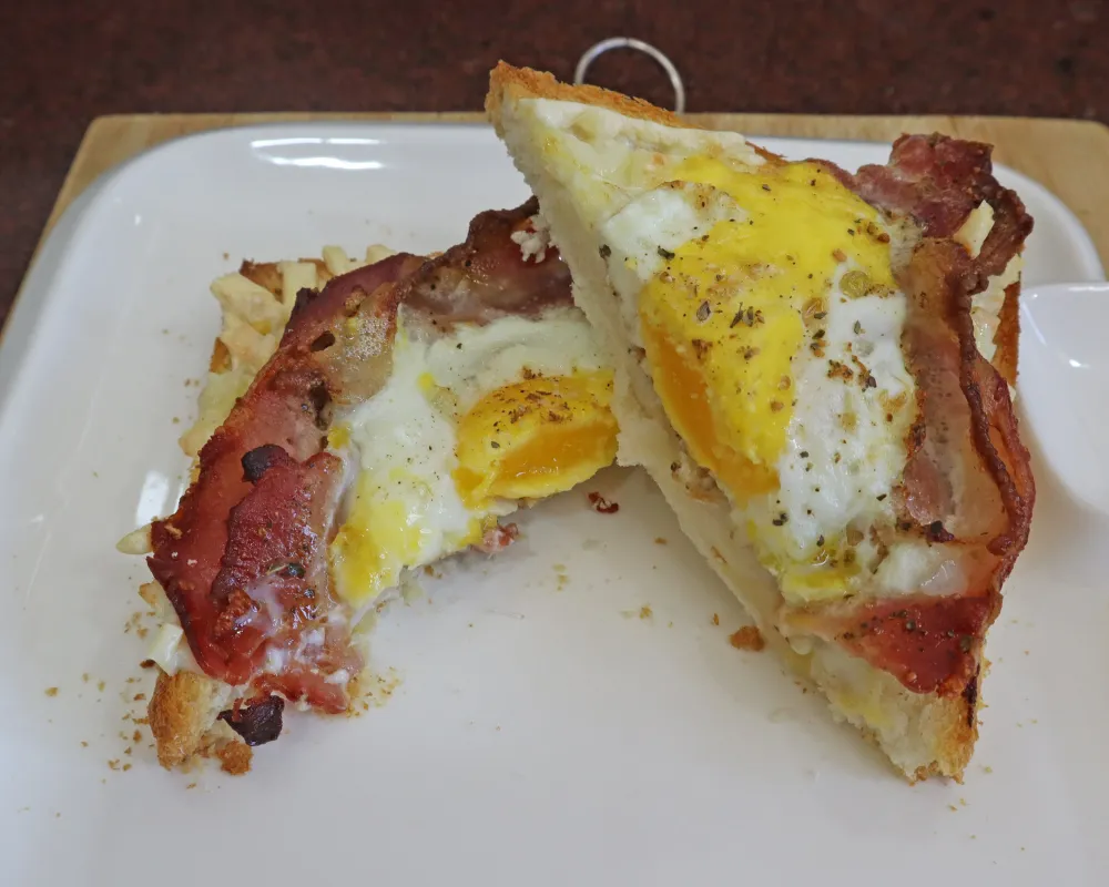 Air fryer bacon and egg toast cut in half on a white plate with the yolk running