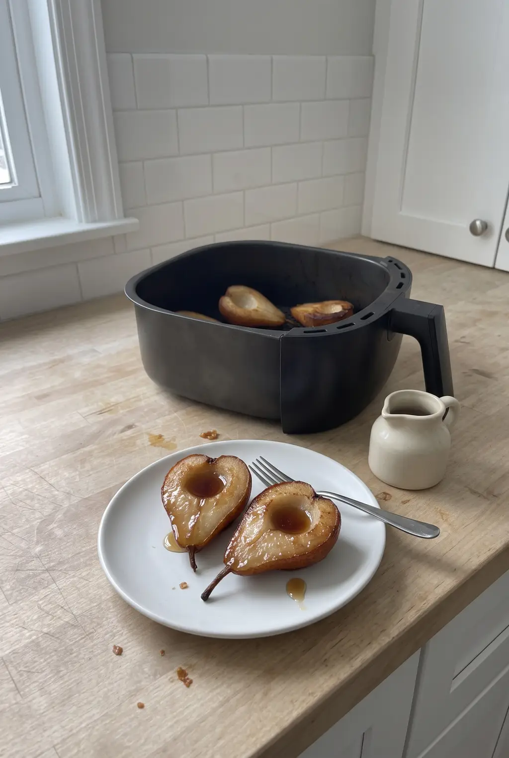 A caramelized air fryer baked pear half on a white plate with maple drizzle and a fork