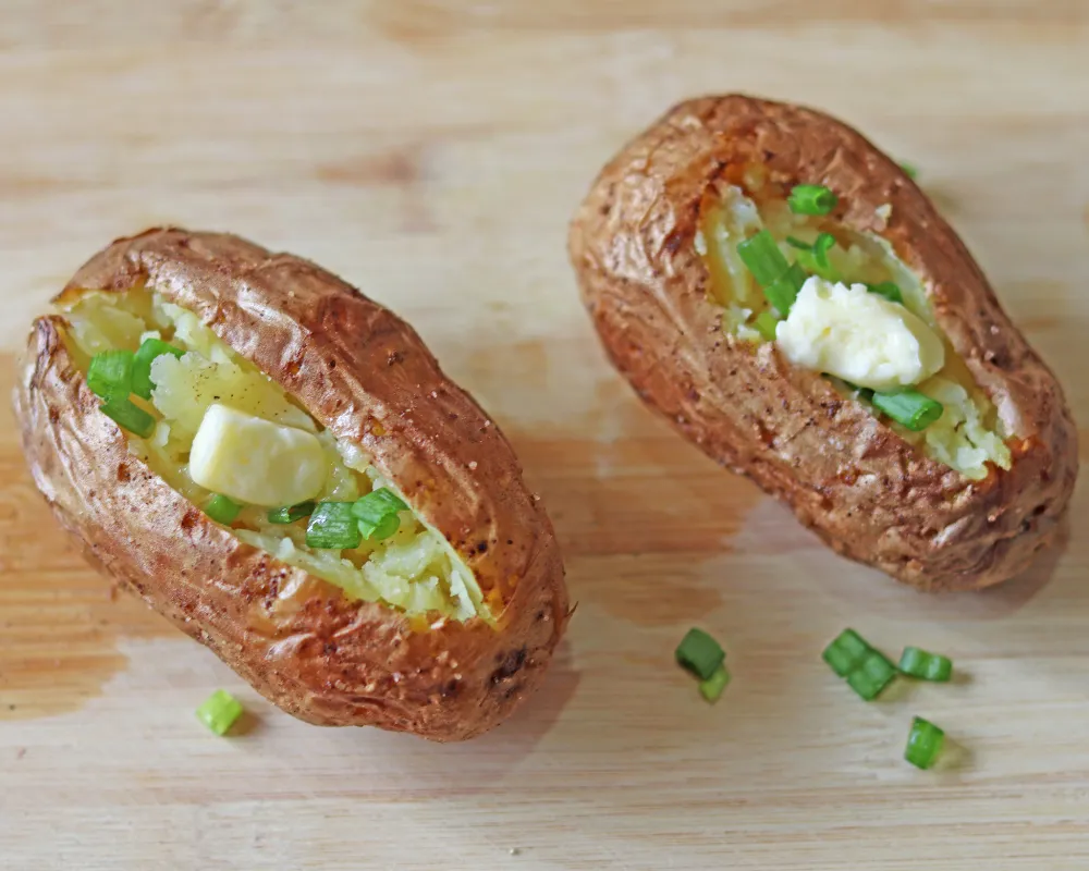 Two air fryer baked potatoes split open with butter melting into the fluffy centers and chopped chives on top