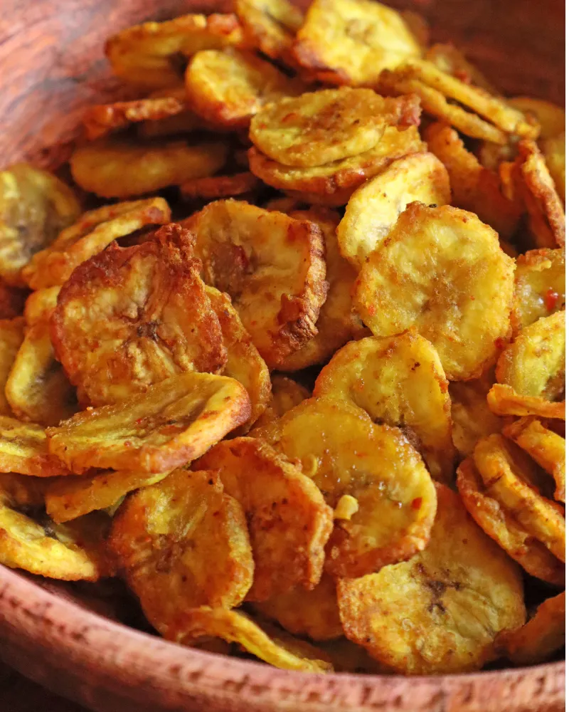 A wooden bowl of golden air fryer banana chips seasoned with turmeric and chili