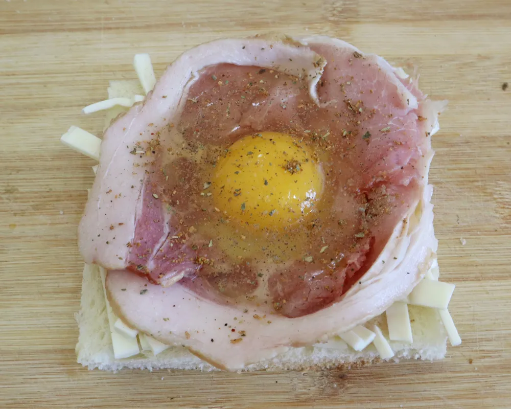 An egg cracked into the middle of the bacon ring and seasoned with pepper and dried herbs