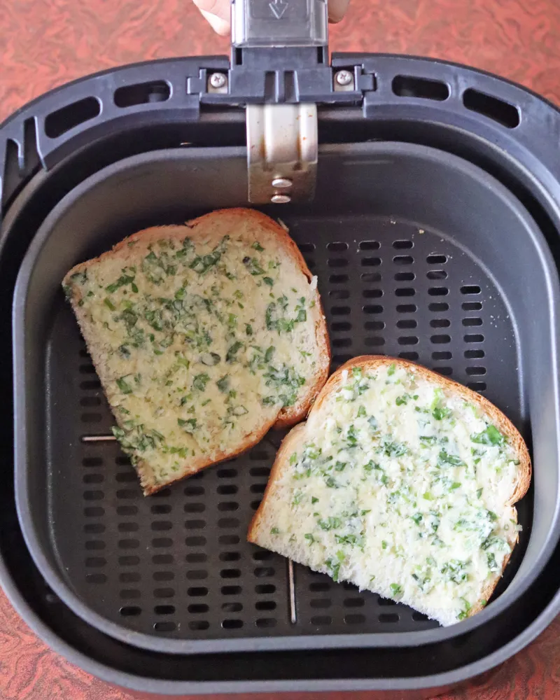 Two slices of bread spread with garlic parsley butter, butter side up on a bare air fryer basket