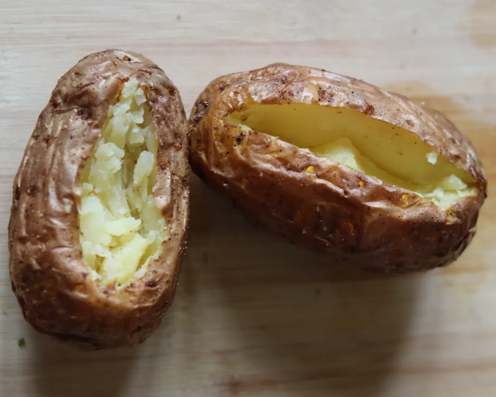 Two cooked baked potatoes split open showing crisp brown skin and a pale fluffy interior