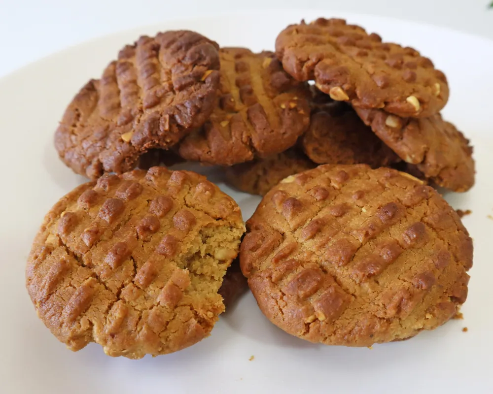 A plate piled with air fryer peanut butter cookies, fork crosshatch on every top, one with a bite taken