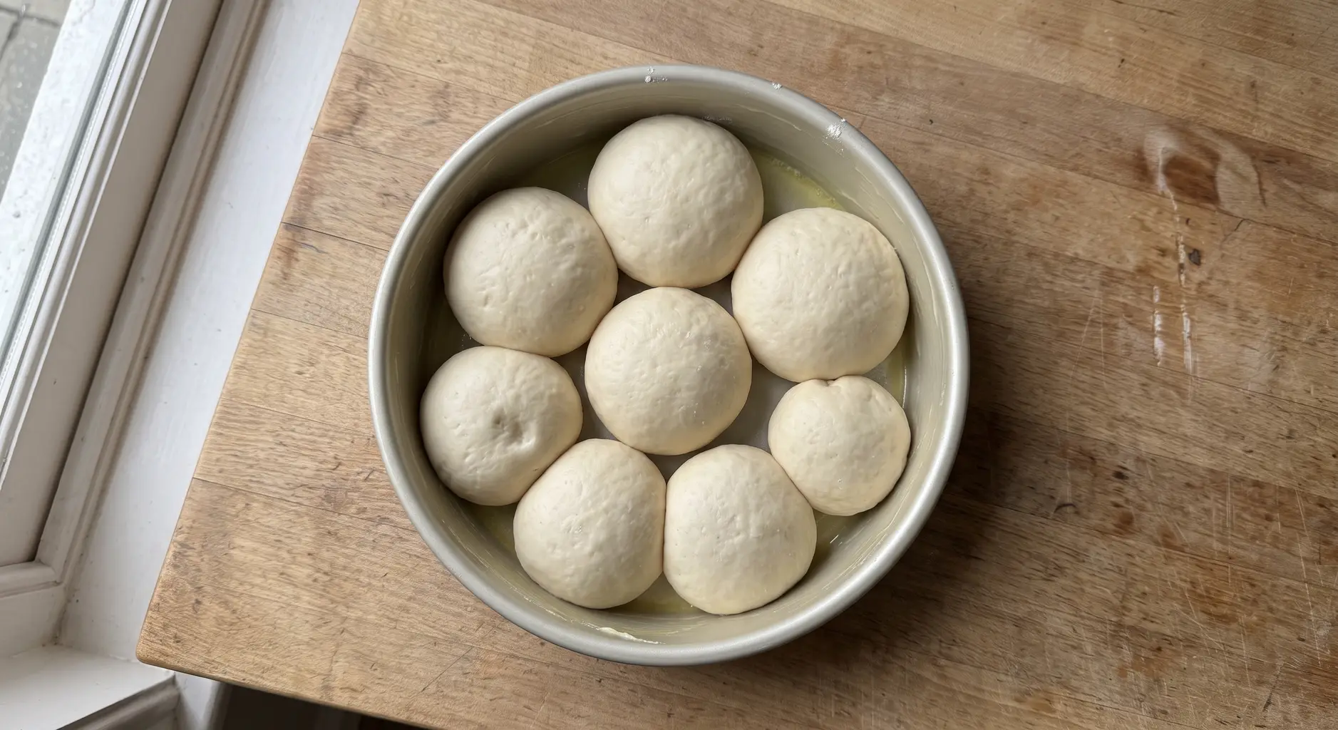 Eight shaped dough balls arranged touching in a buttered round cake pan, seven around one in the middle