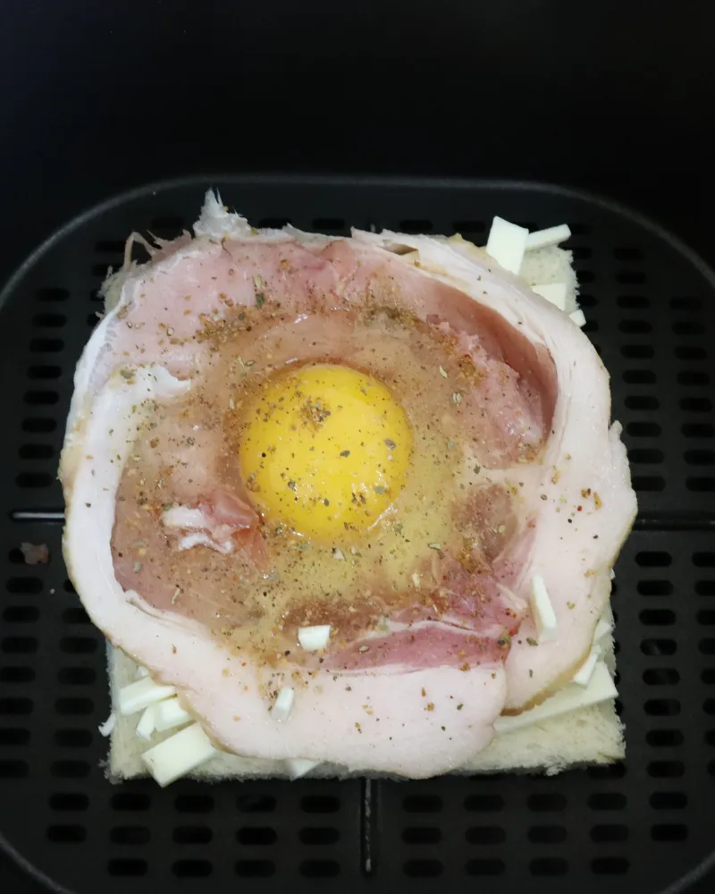 The assembled bacon and egg toast sitting on the perforated floor of an air fryer basket