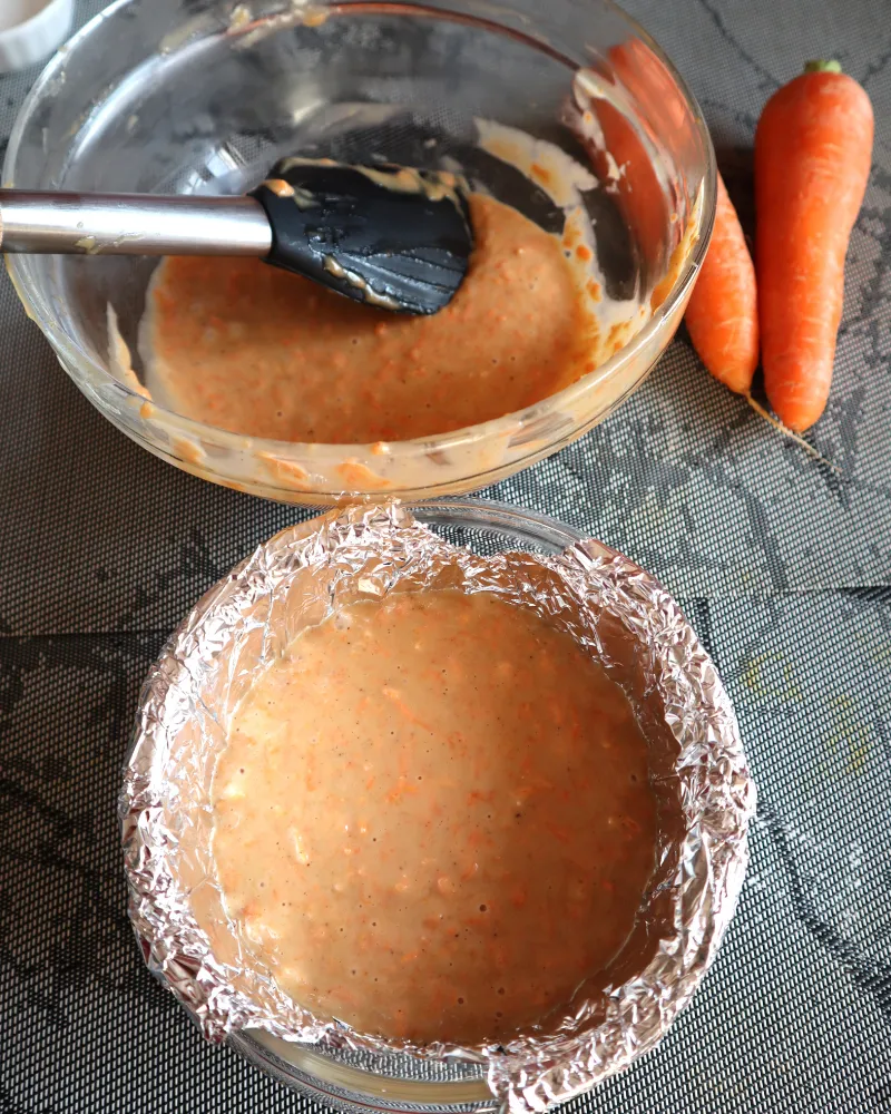Finished carrot cake batter in a bowl beside a foil-lined pan filled with batter