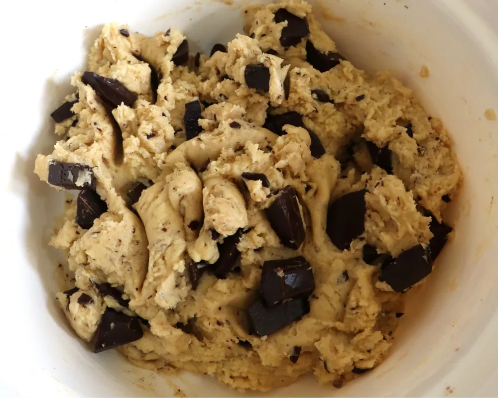 Chocolate chip cookie dough in a white bowl with large chopped chocolate chunks throughout