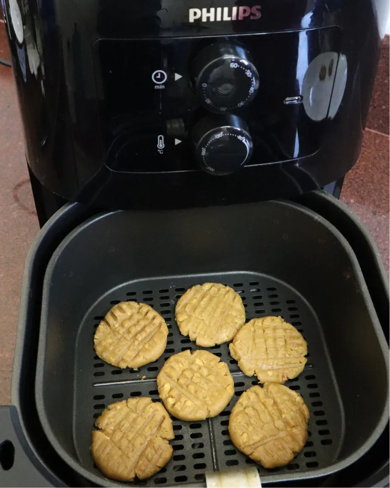 Six crosshatched peanut butter cookies arranged in an air fryer basket before baking