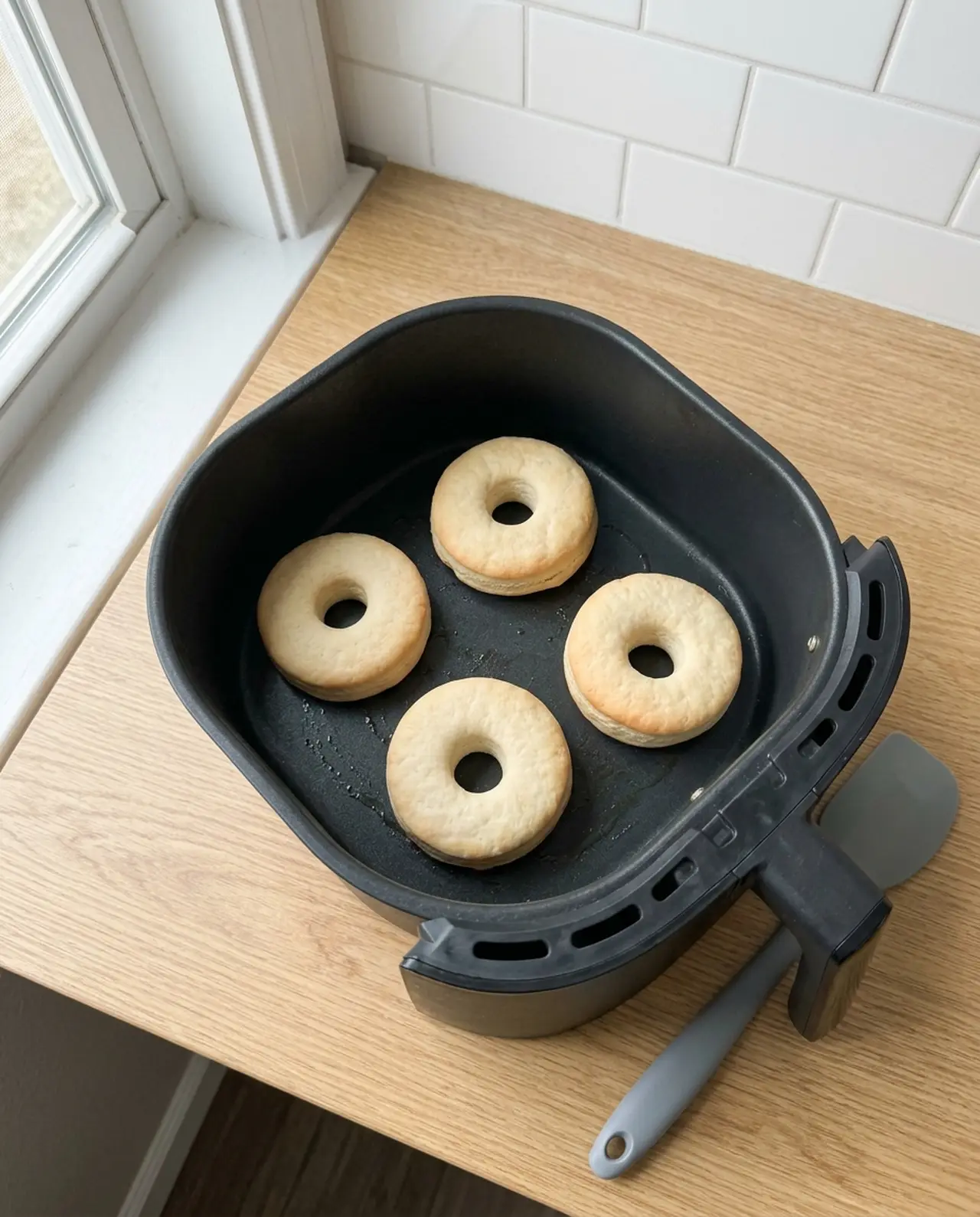 Four air fryer biscuit donuts baked to light golden in the basket