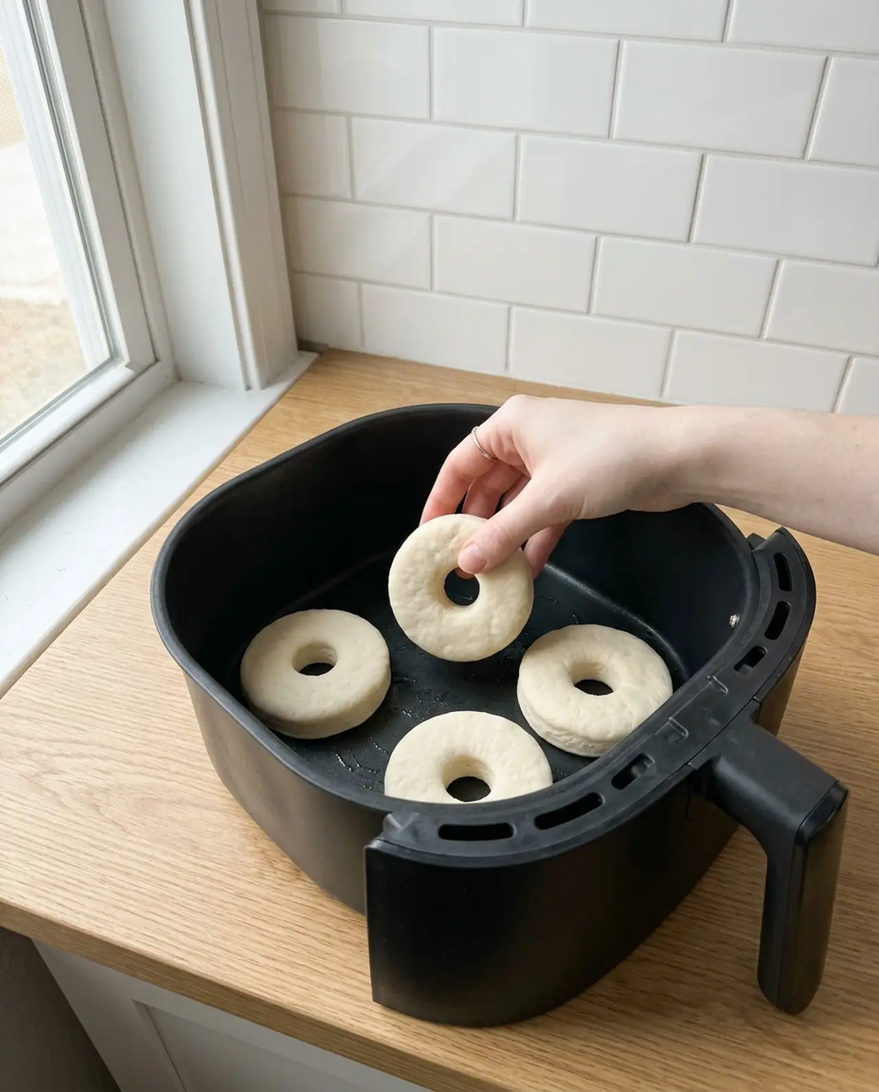 Four raw canned biscuit donut rings arranged with space between them in an air fryer basket