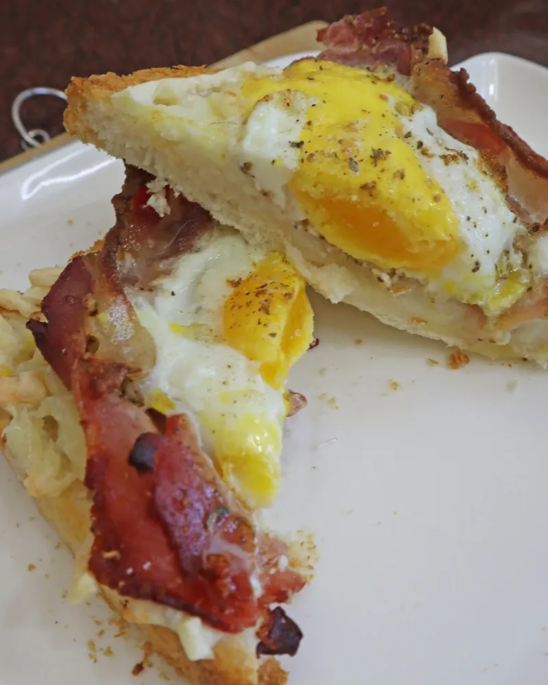 Two halves of air fryer bacon and egg toast on a white plate with the yolk running onto the bread
