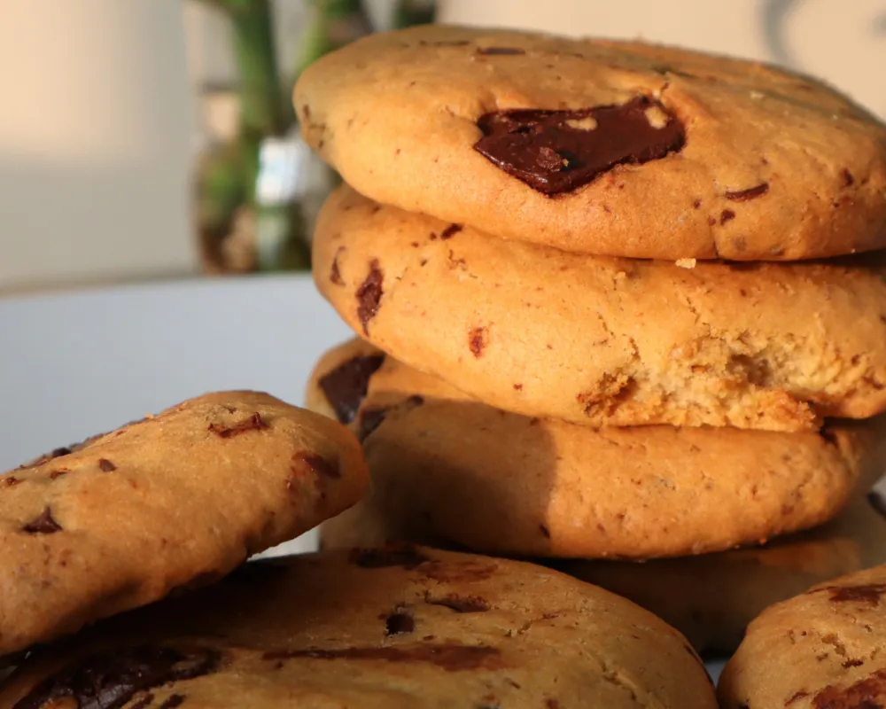 A stack of air fryer chocolate chip cookies with one broken open showing a soft interior crumb