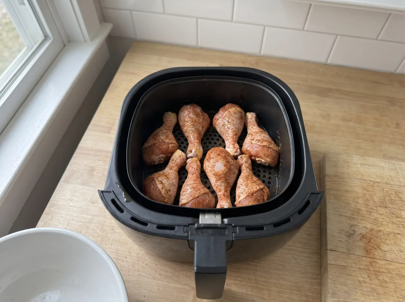 Seasoned chicken drumsticks arranged in a single spaced layer in the air fryer basket