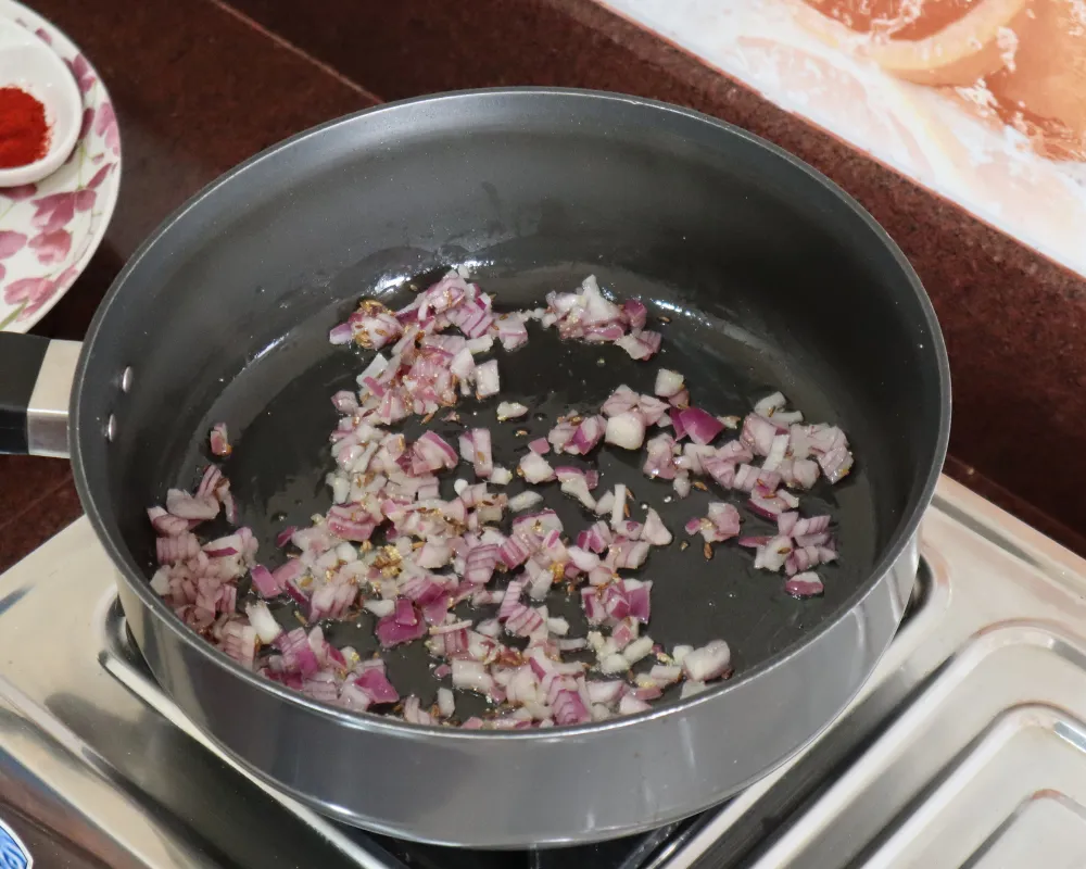 Chopped red onion frying with cumin seeds in oil in a steel pan