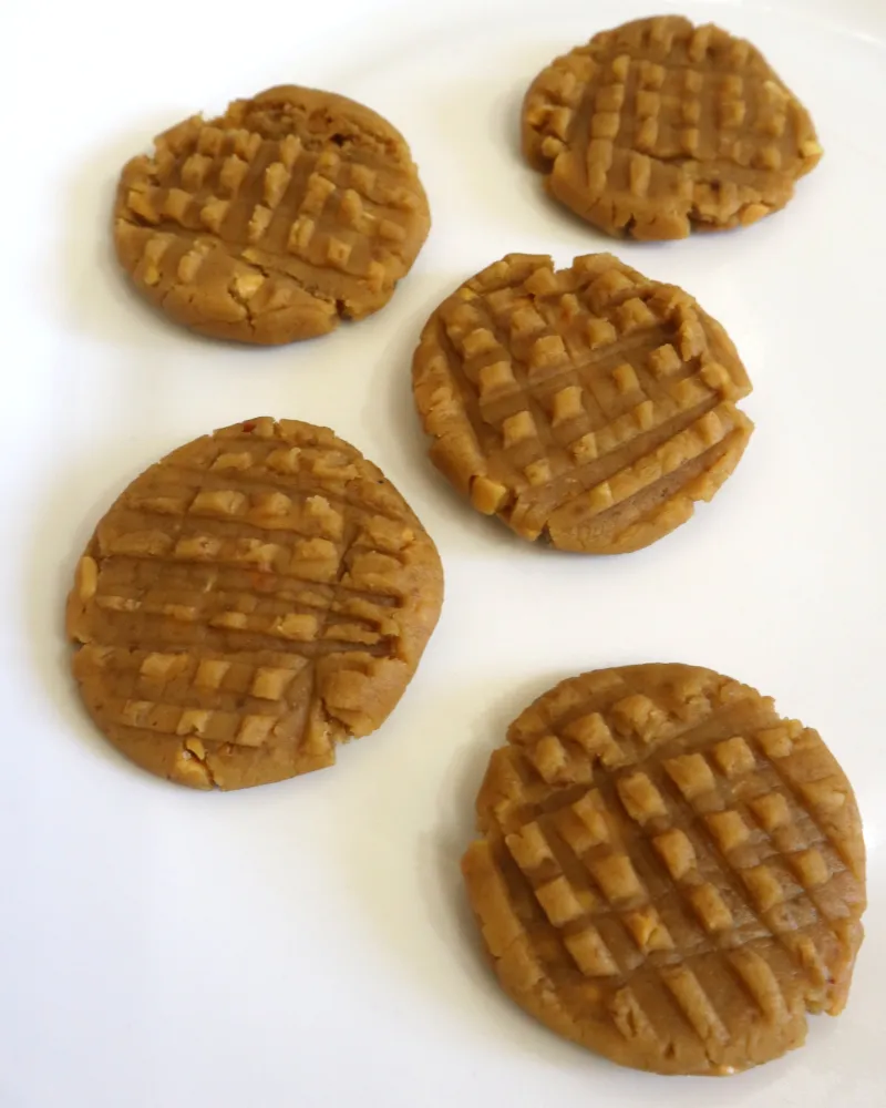 Five raw peanut butter cookies on a white plate with deep fork crosshatch marks