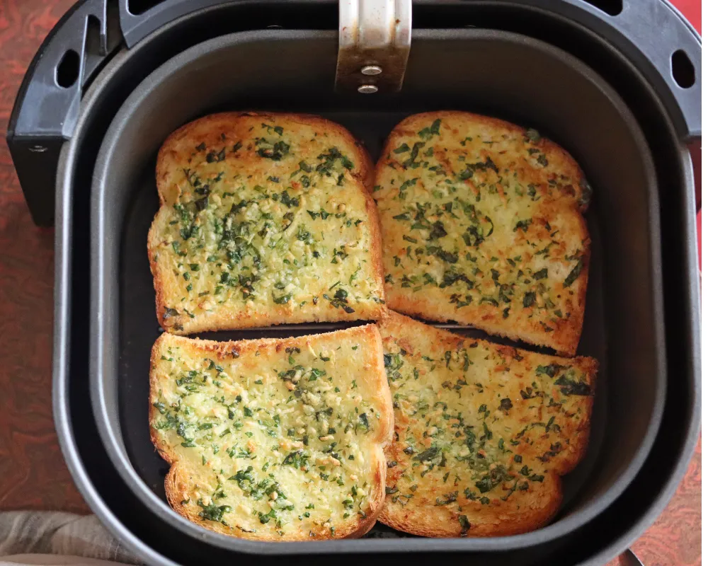 Four golden, crisp slices of garlic bread in an air fryer basket after baking