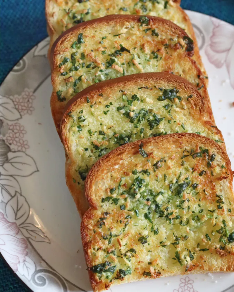 Golden air fryer garlic bread slices with parsley and toasted garlic butter lined up on a plate