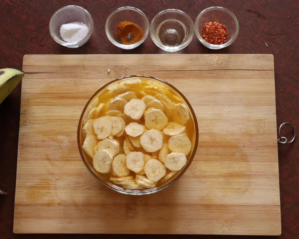 Green banana slices soaking in a bowl of yellow turmeric water