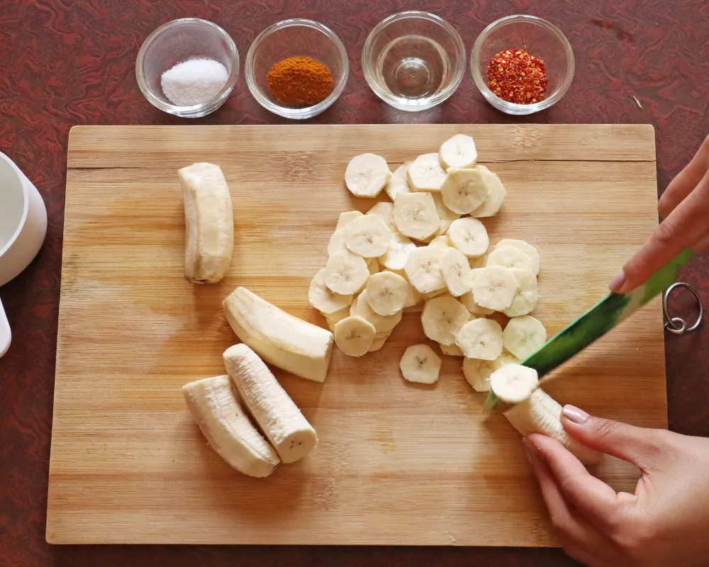 Slicing peeled green bananas into rounds on a wooden board