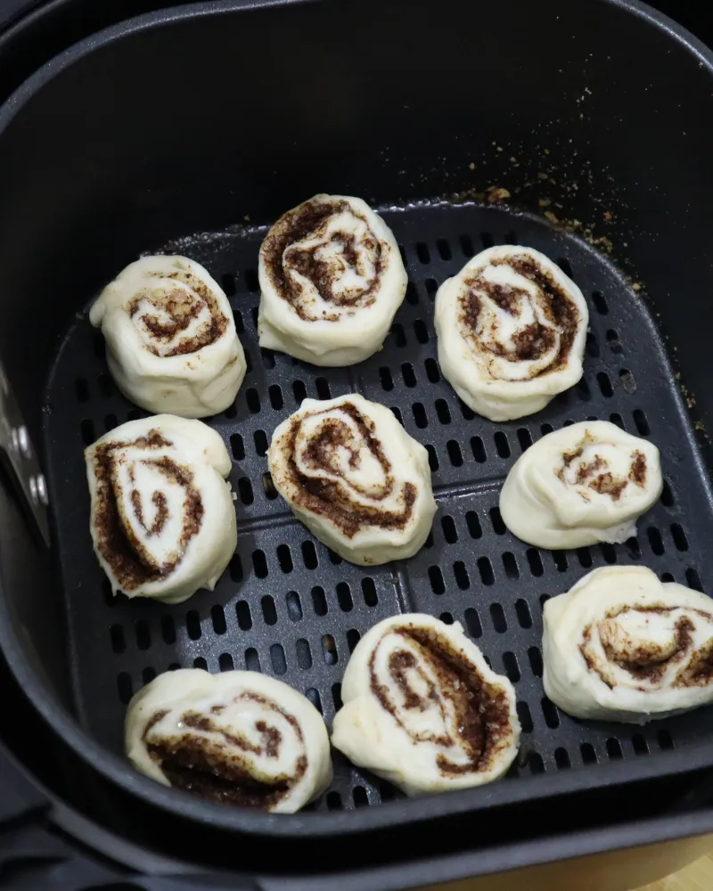 Nine raw hand cut cinnamon rolls arranged spiral side up in an air fryer basket