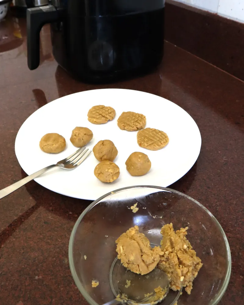Plate of rolled peanut butter cookie dough balls and pressed cookies with a fork, air fryer behind