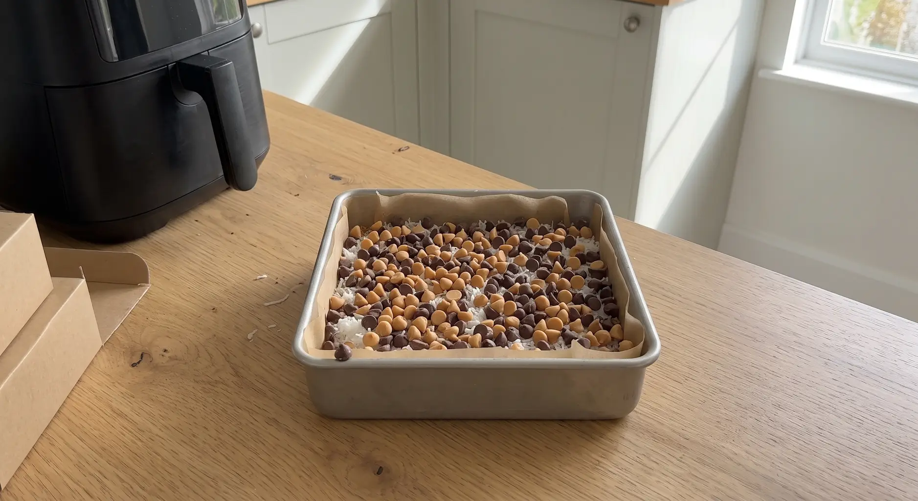 Chocolate chips and butterscotch chips scattered edge to edge over a coconut layer in a lined pan
