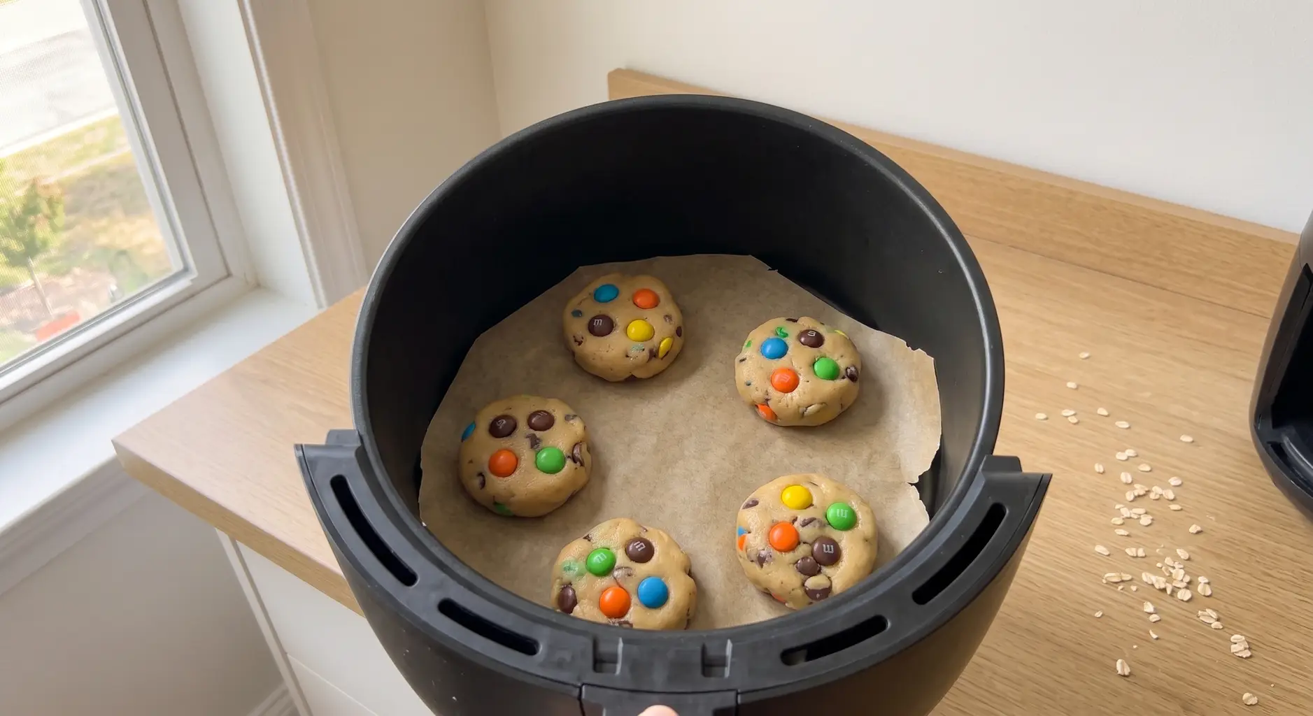 Five scooped monster cookie dough mounds spaced on parchment in an air fryer basket