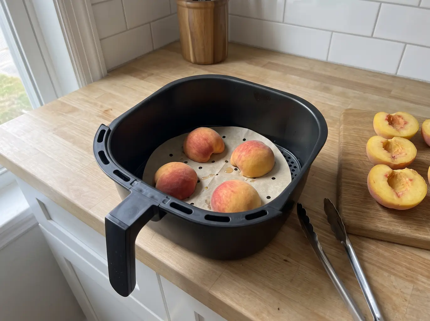 Peach halves set cut side down on perforated parchment in an air fryer basket