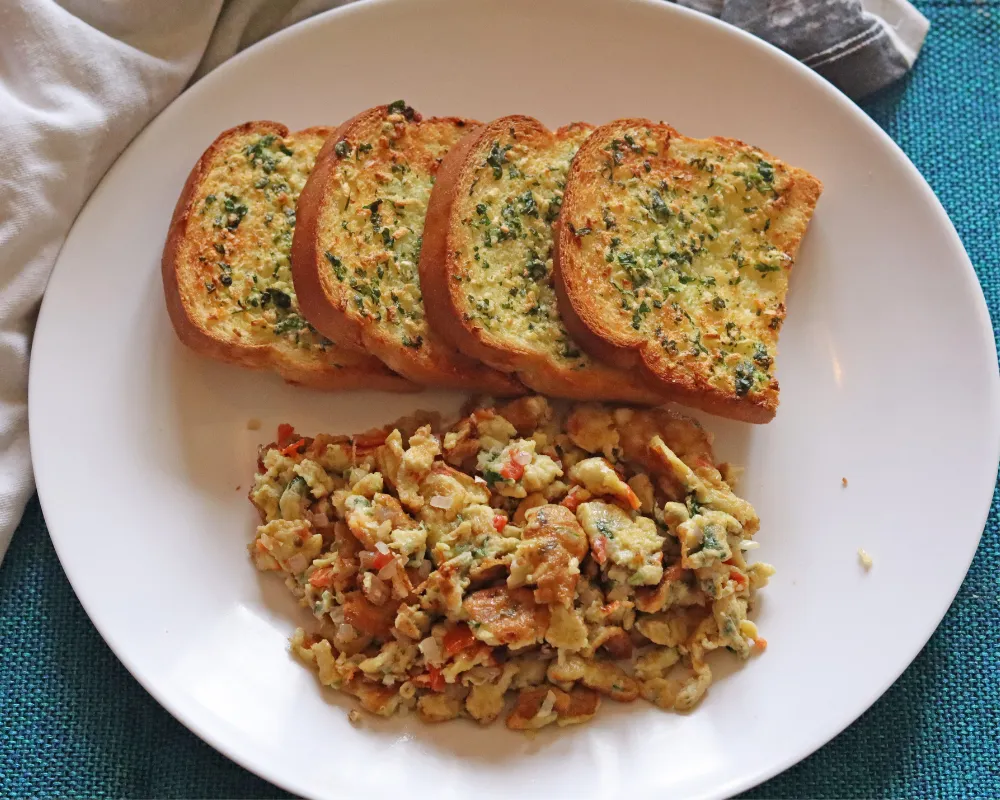 Air fryer garlic bread slices on a plate beside scrambled eggs