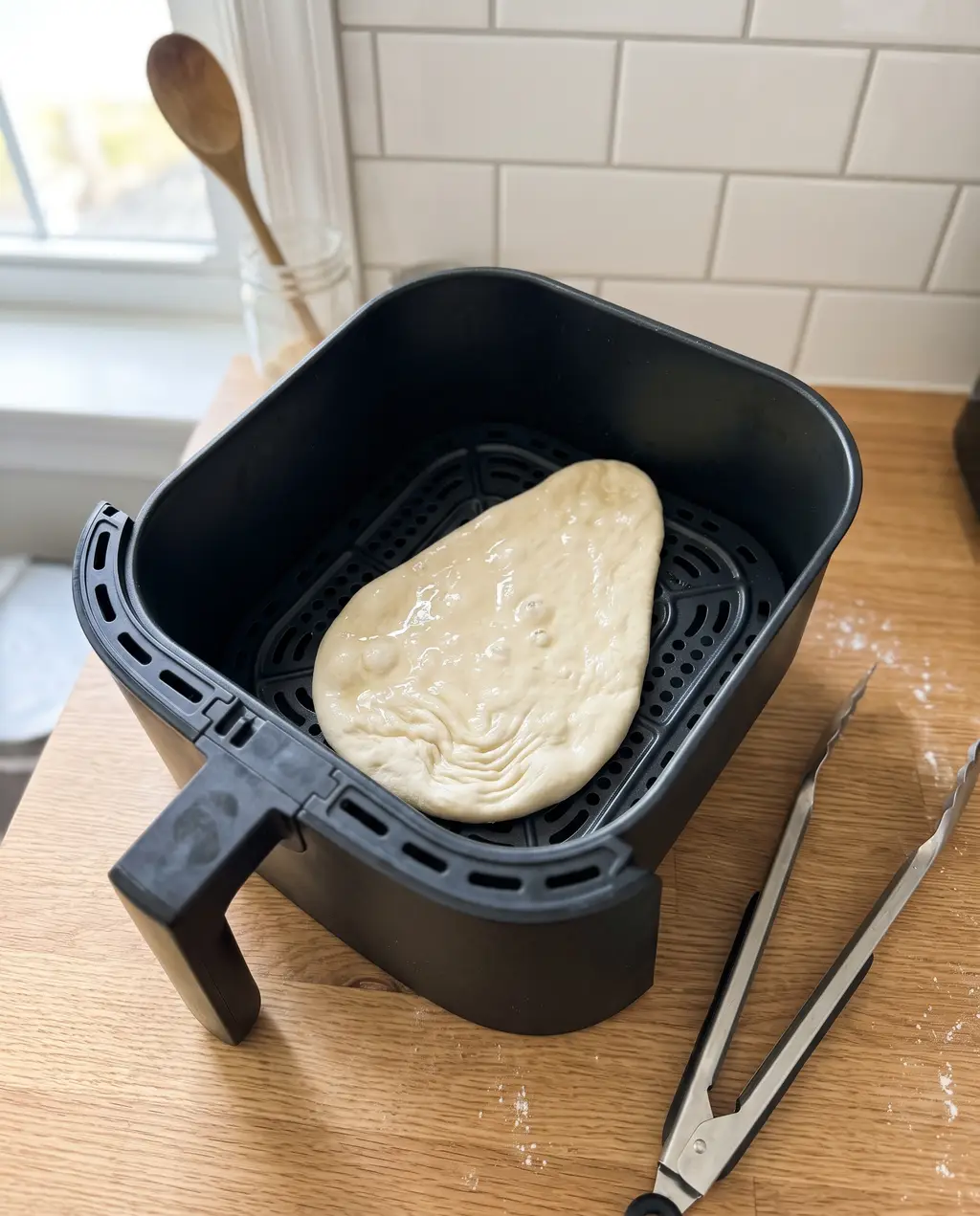 Raw, water-sheened naan dough laid directly on the bare perforated floor of a preheated air fryer basket