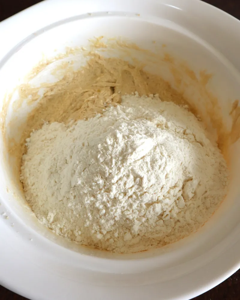 Flour added on top of wet cookie batter in a white mixing bowl before folding
