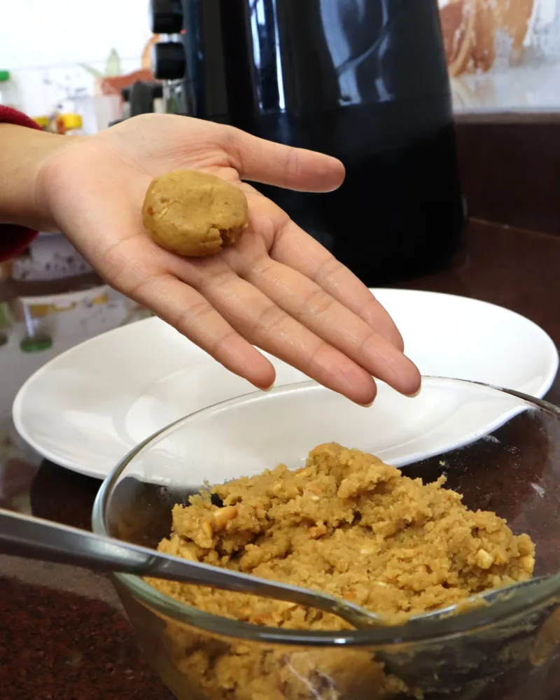 A hand holding one rolled ball of peanut butter cookie dough above the mixing bowl