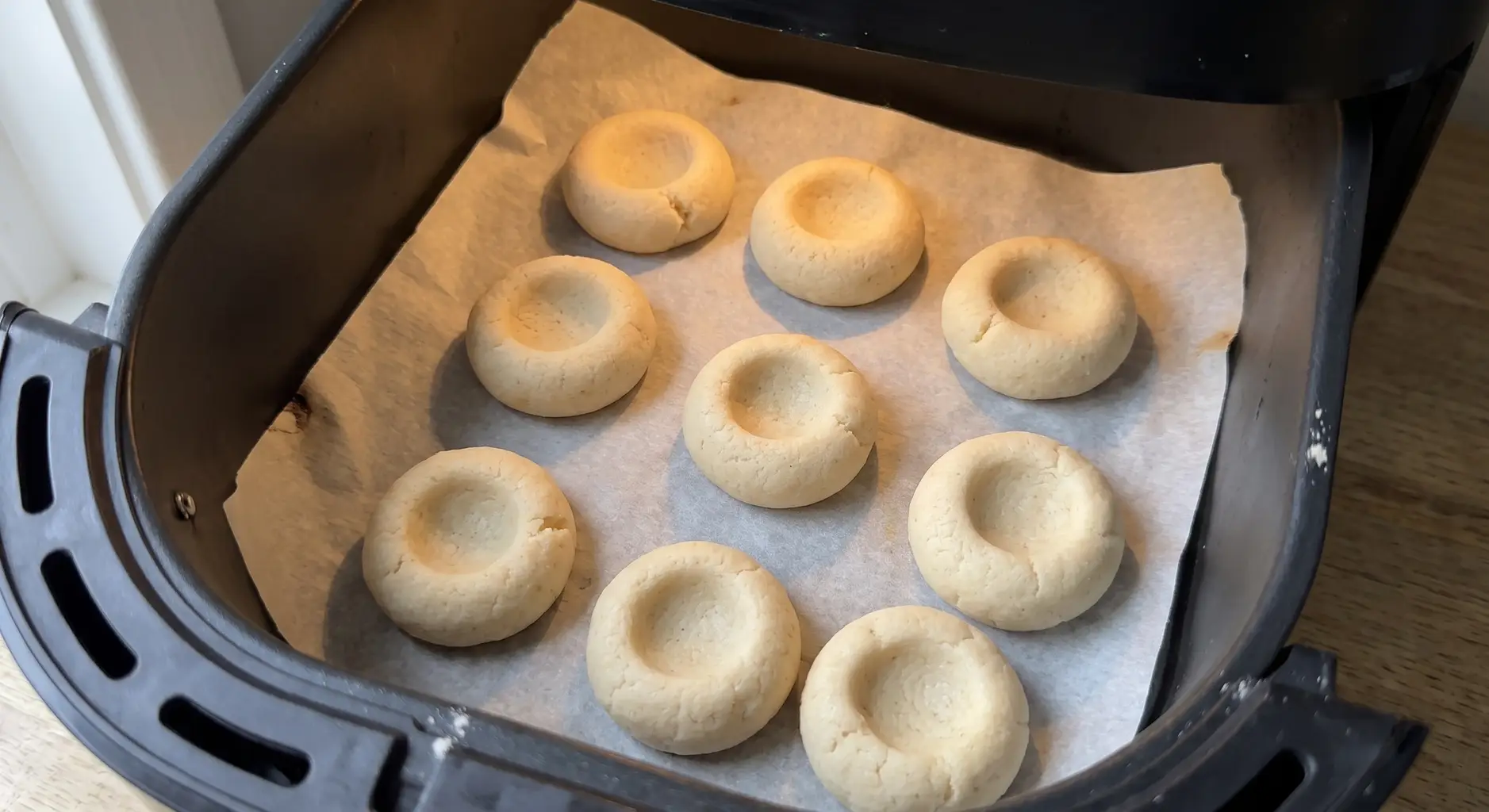 Unfilled thumbprint cookies baking on parchment in an air fryer basket