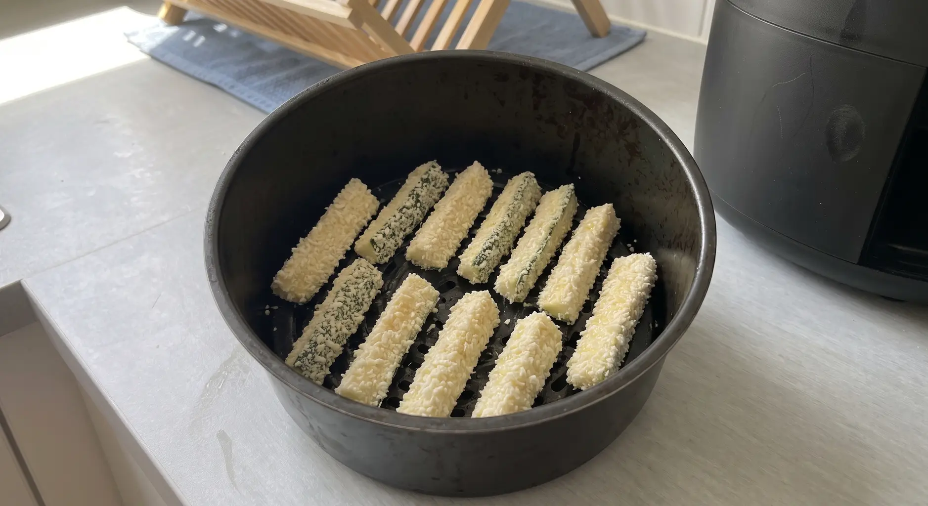 Breaded zucchini sticks arranged in a single layer with gaps in an air fryer basket